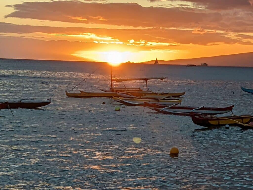 orange sun setting in the ocean behind outrigger canoes
